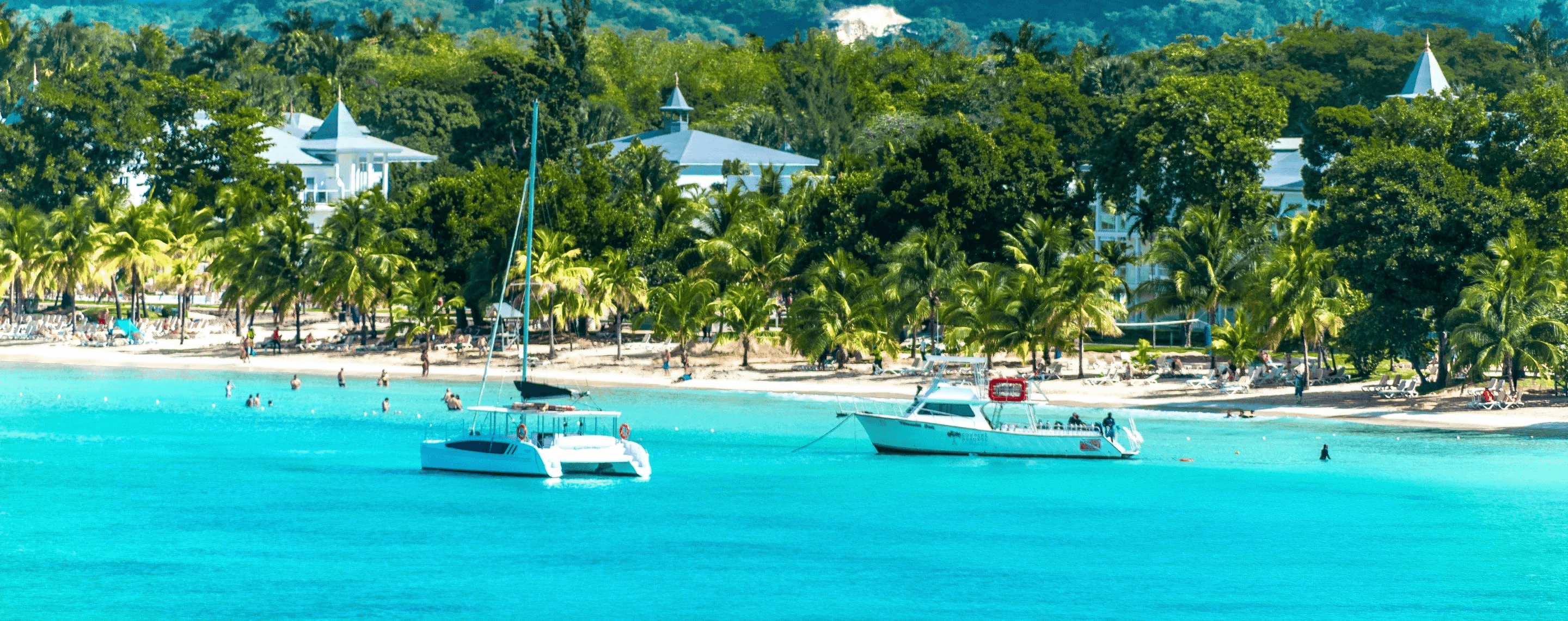 Boote, Palmen und türkisfarbenes Wasser am Strand von Negril auf Jamaika